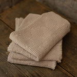 Stack of taupe towels on a wooden surface with a stone wall background