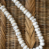 White beaded necklace with small blue eyes on a wicker background
