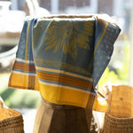 Decorative towel with sunflower pattern draped over a wooden stool outdoors.