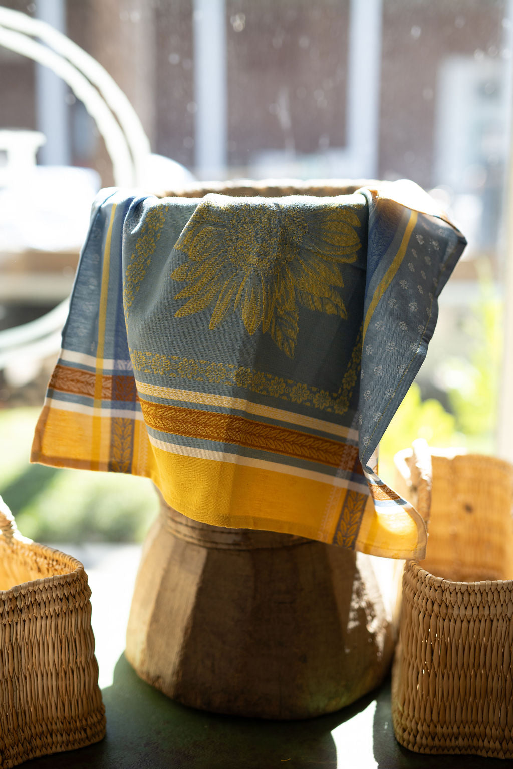 Decorative towel with sunflower pattern draped over a wooden stool outdoors.