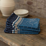 Stack of blue patterned napkins on a wooden surface with a stone wall background