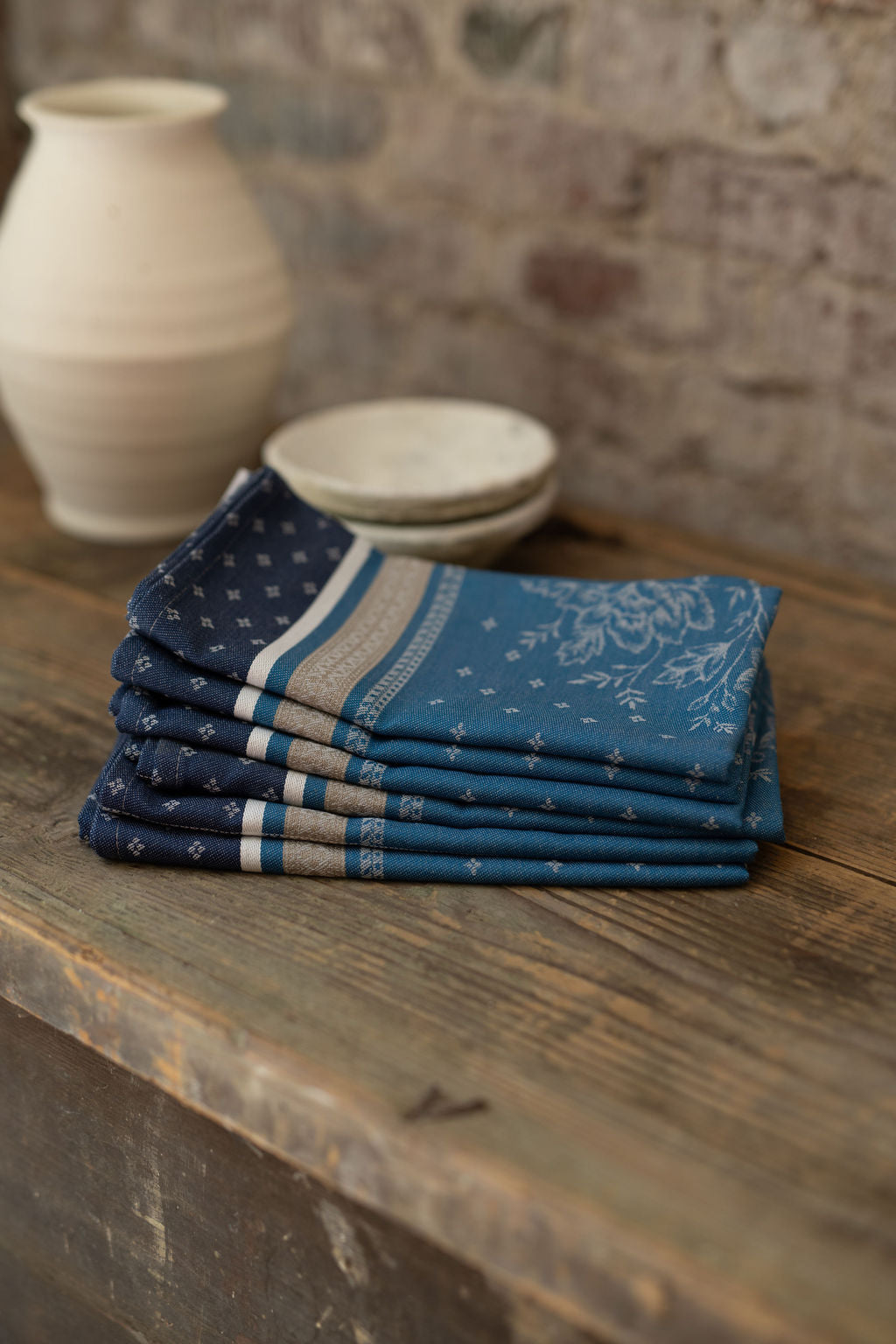 Stack of blue patterned napkins on a wooden surface with a stone wall background