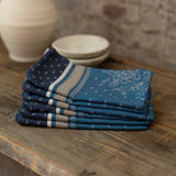 Stack of blue patterned napkins on a wooden surface with a stone wall background