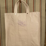 Beige tote bag hanging against a striped background