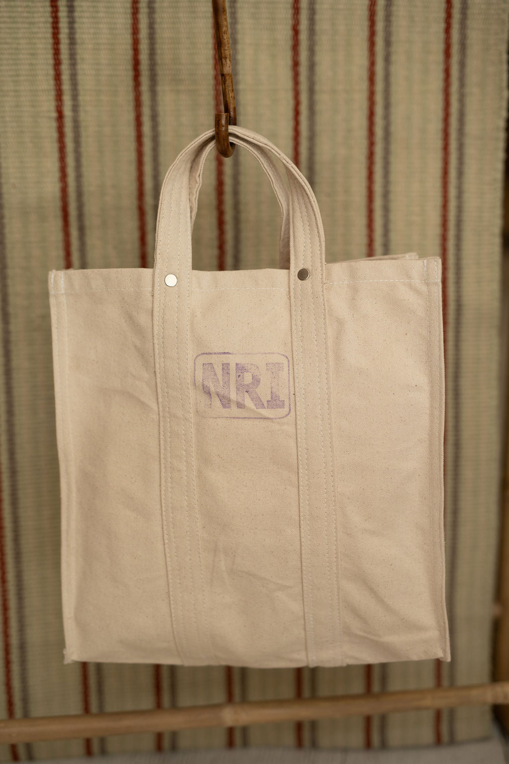 Beige tote bag hanging against a striped background