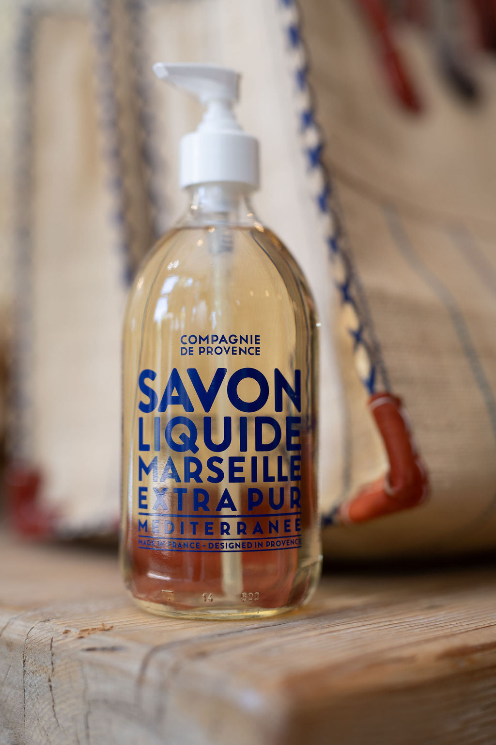 Bottle of Compagnie de Provence Marseille Liquid Soap on a wooden surface with a blurred background.