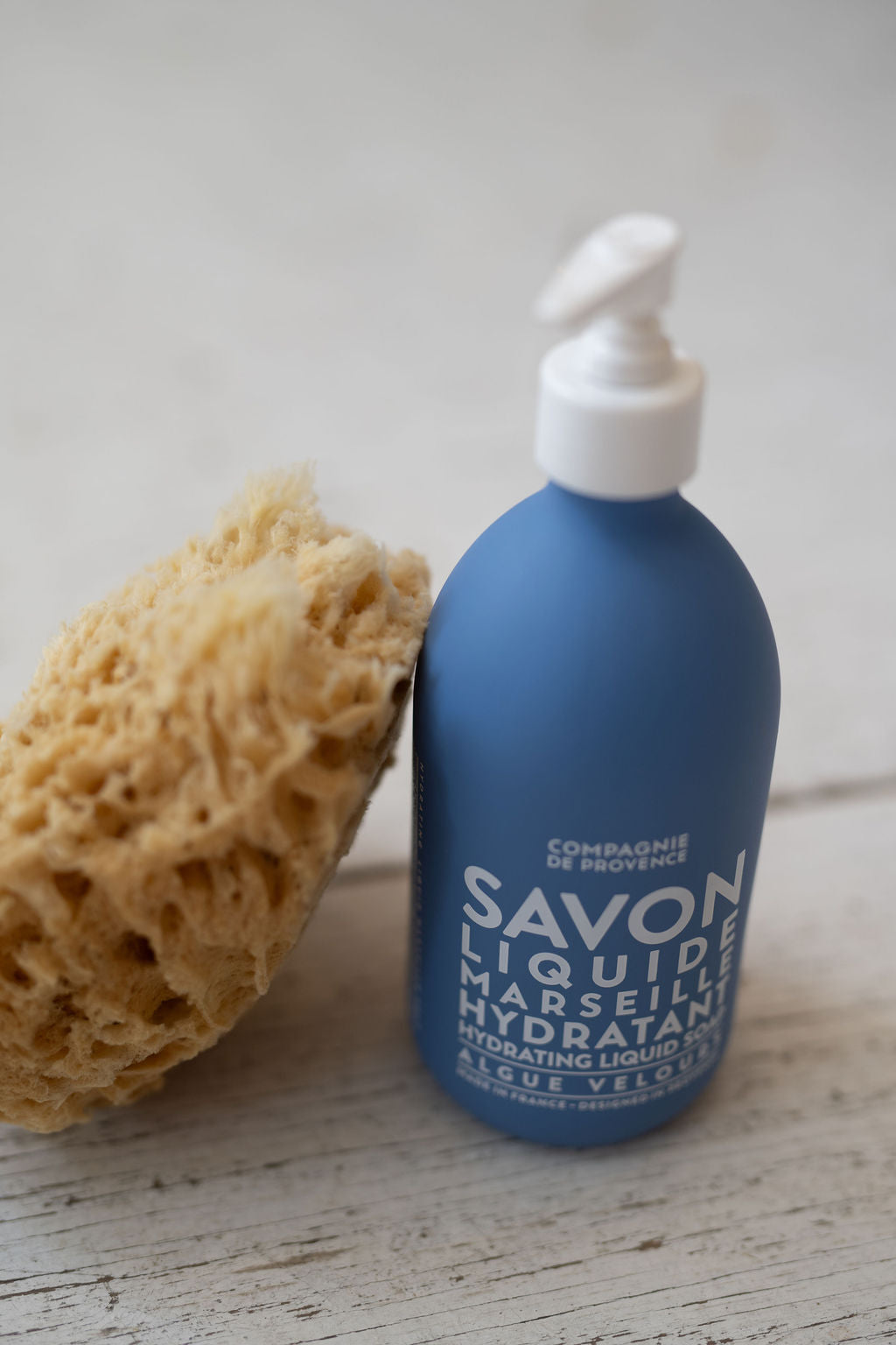 Blue bottle with pump and sponge on a wooden surface