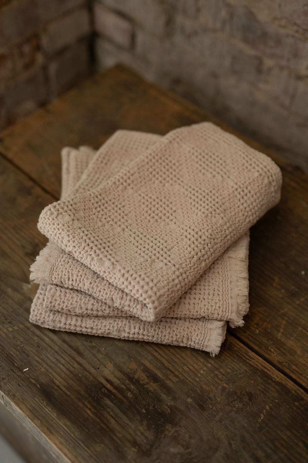 Stack of taupe towels on a wooden surface with a stone wall background