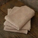 Stack of taupe towels on a wooden surface with a stone wall background