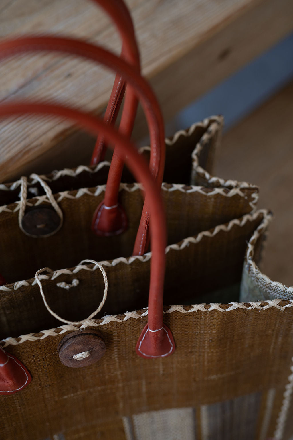 Close-up of a brown leather bag with red handles on a wooden surface