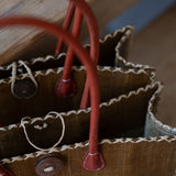 Close-up of a brown leather bag with red handles on a wooden surface