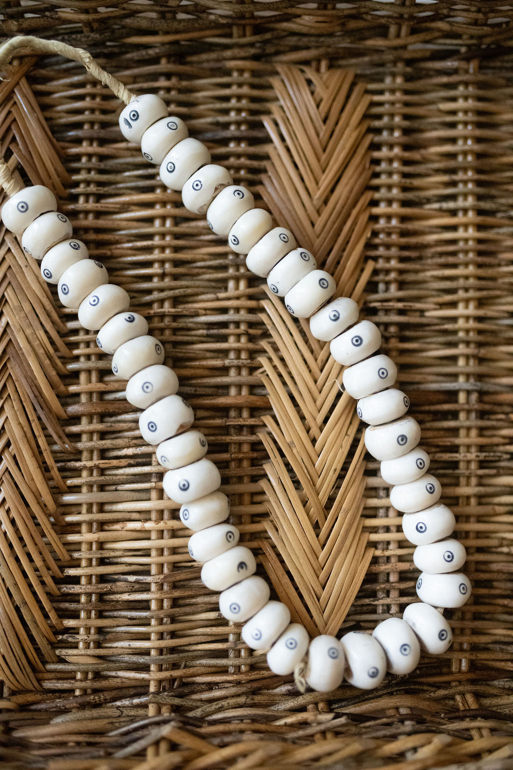 White beaded necklace with small blue eyes on a wicker background